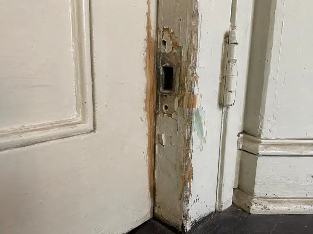 Paint worn through to bare wood on a door edge next to the strike plate, layers of older paint visible