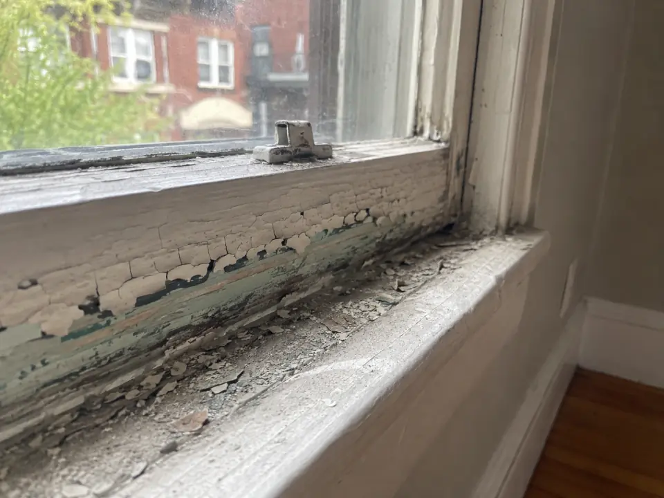 Cracked and peeling paint on an old wooden window sash and sill