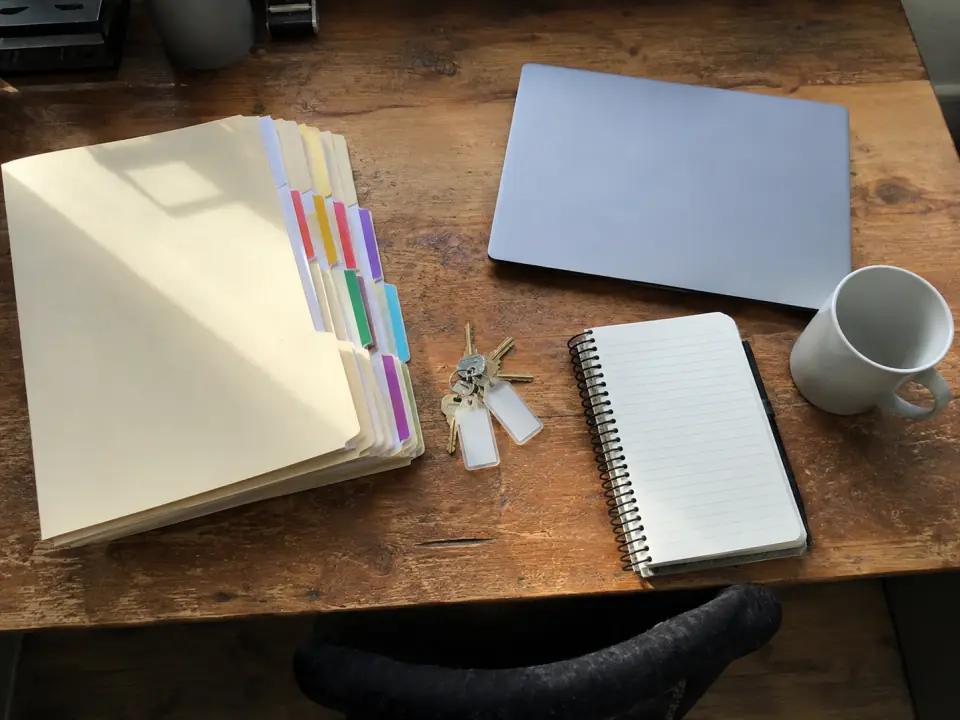 A property manager's desk with lease folders, unit keys, a notebook and a laptop