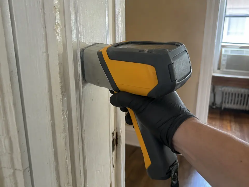 A handheld XRF analyzer held against painted door trim in an old apartment